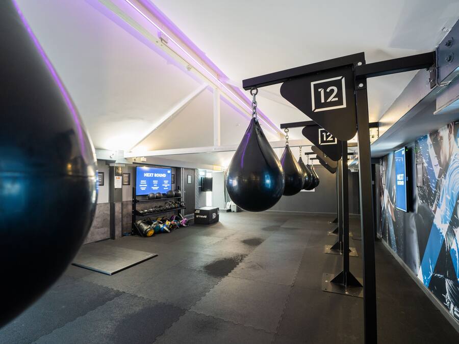 Een sportschool met bokszakken, een digitaal scherm en een muur met een poster.