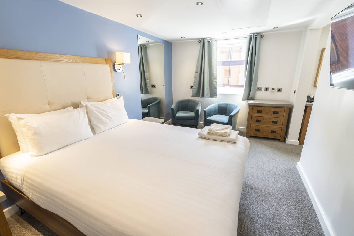 Ein Hotelzimmer mit einem großen Bett, zwei Sesseln, einer kleinen Holzkabine und einem Spiegel an der Wand.
