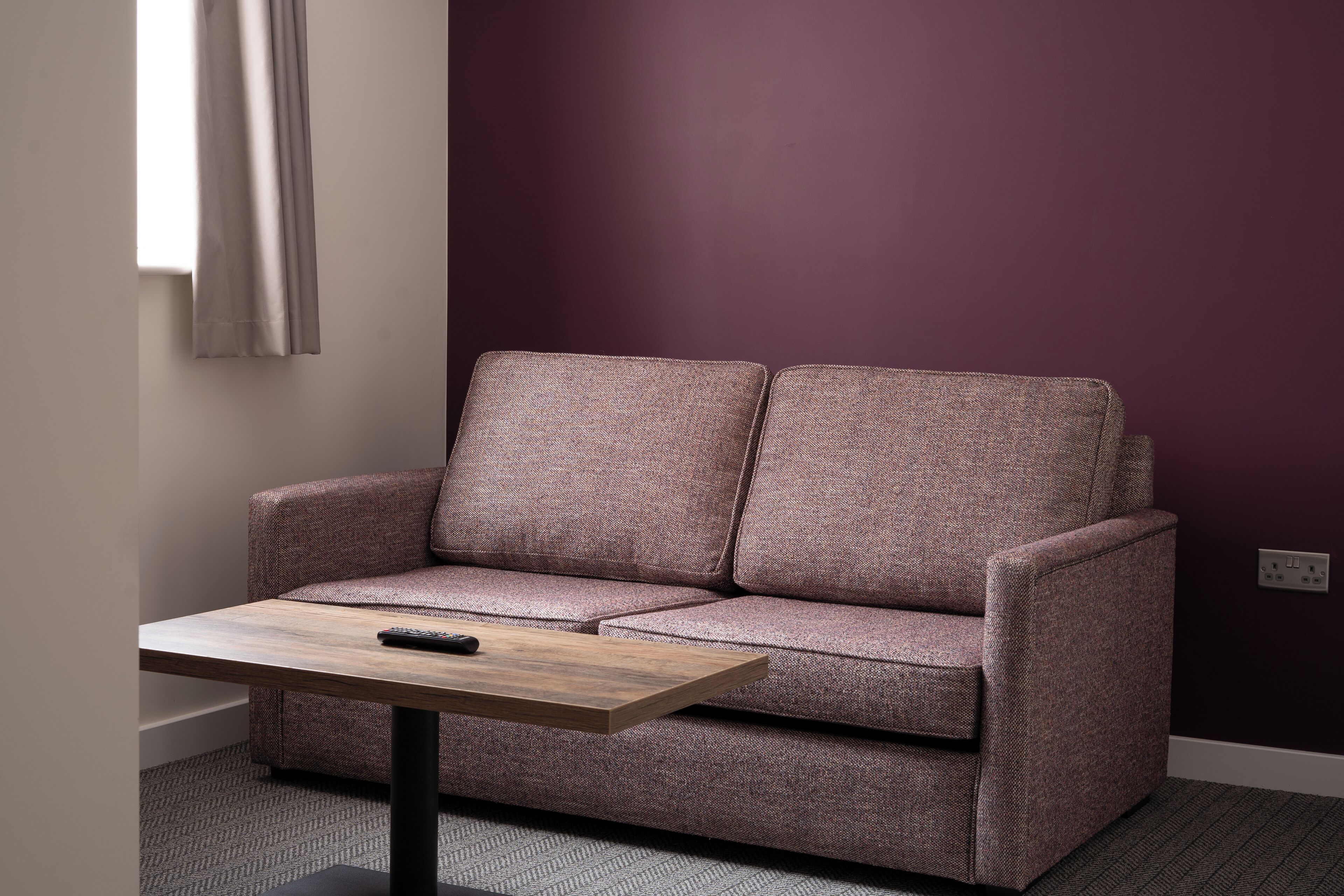 Ein Zimmer mit einer Couch, einem kleinen Tisch und einer violetten Wand.