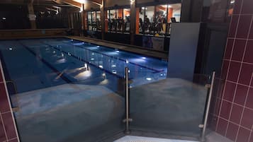 Una amplia piscina cubierta con zona de hidromasaje, rodeada por un muro de azulejos y una barrera de cristal.