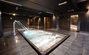 A modern indoor pool area with a central hot tub, surrounded by dark tiled walls and a polished floor. - Waterside Hotel & Leisure Club (Manchester)