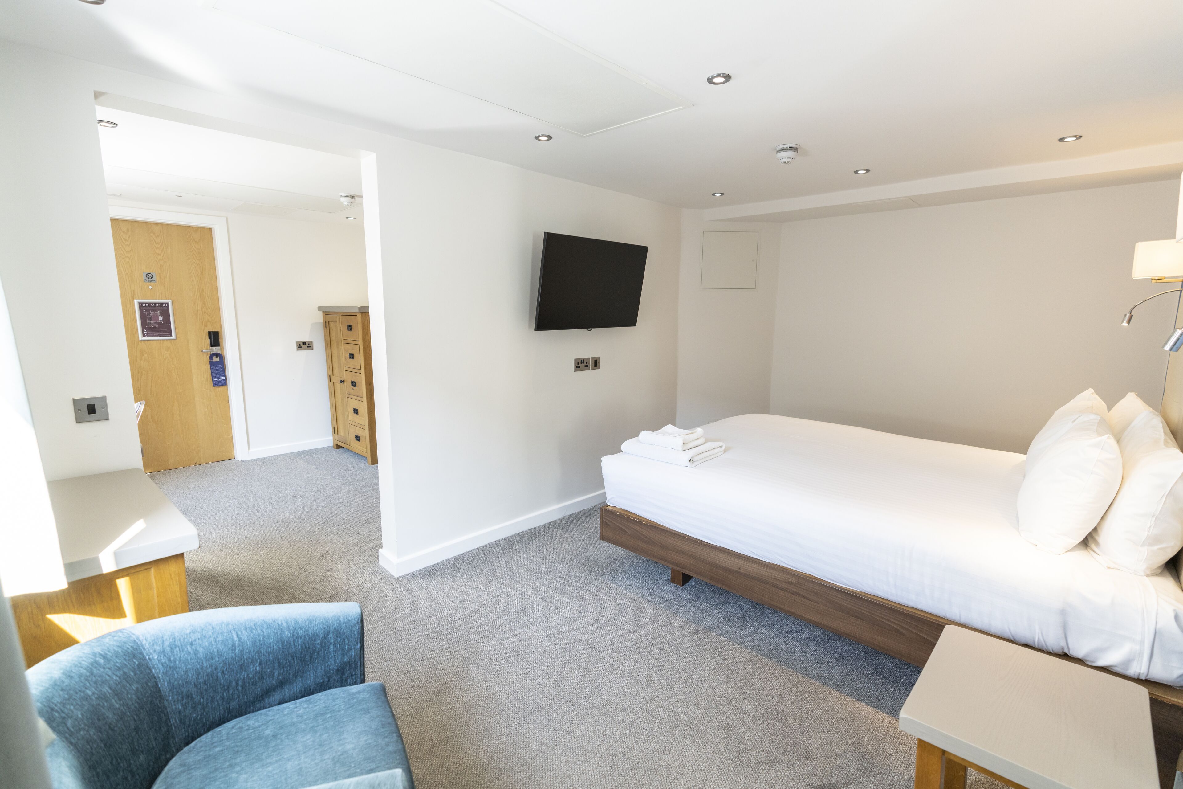 A hotel room with a bed, a desk, a chair, a TV, and a door leading to a bathroom.