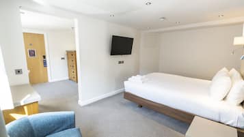 A hotel room with a bed, a desk, a chair, a TV, and a door leading to a bathroom.