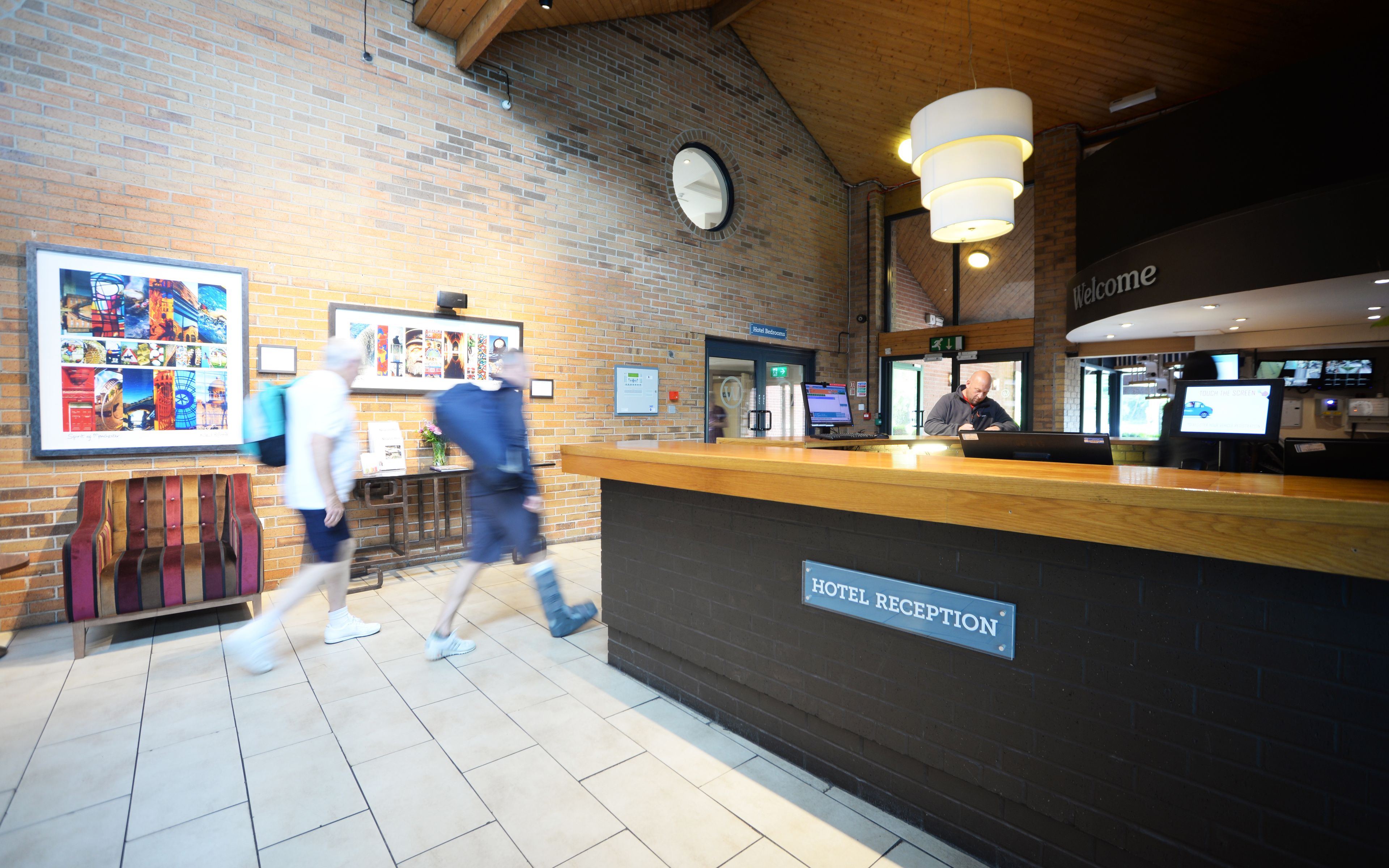 A hotel reception area with a wooden reception desk, a clock, and a sign indicating hotel bedrooms.