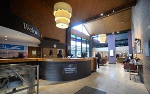 A hotel reception area with a curved counter, a clock, and a sign indicating a leisure club reception. - Waterside Hotel & Leisure Club (Manchester)