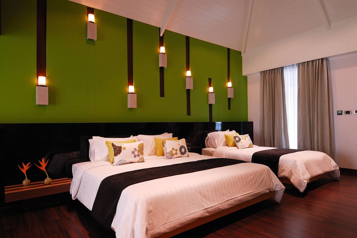 Habitación de hotel con dos camas, una pared de acento verde y luces fijadas a la pared.