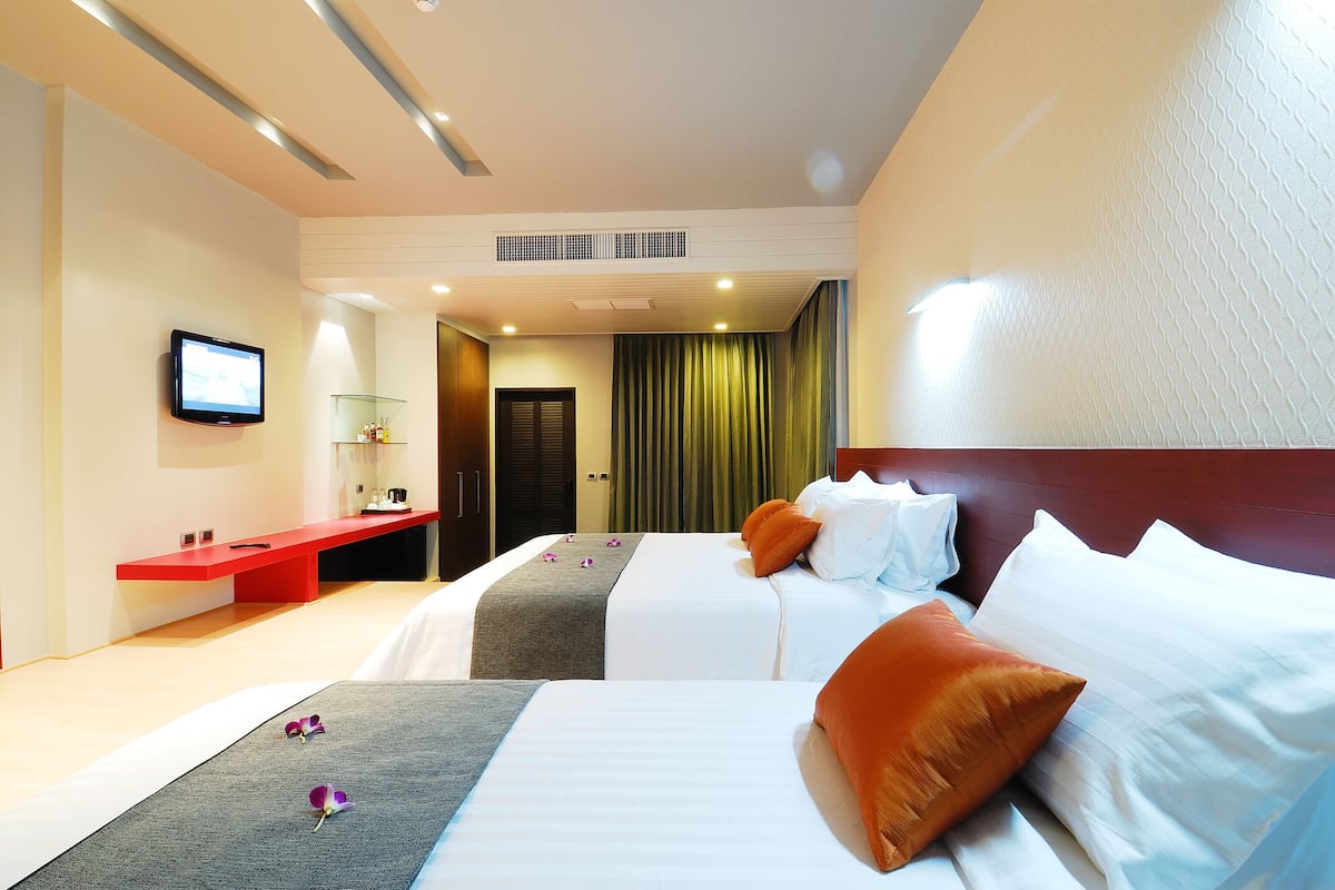 Una habitación de hotel con dos camas, un televisor, un escritorio rojo y un baño visible a través de una puerta abierta.