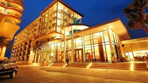 A modern hotel with a glass facade, multiple balconies, and a well-lit entrance. - Long Beach Garden Hotel and Pavilions (Pattaya)