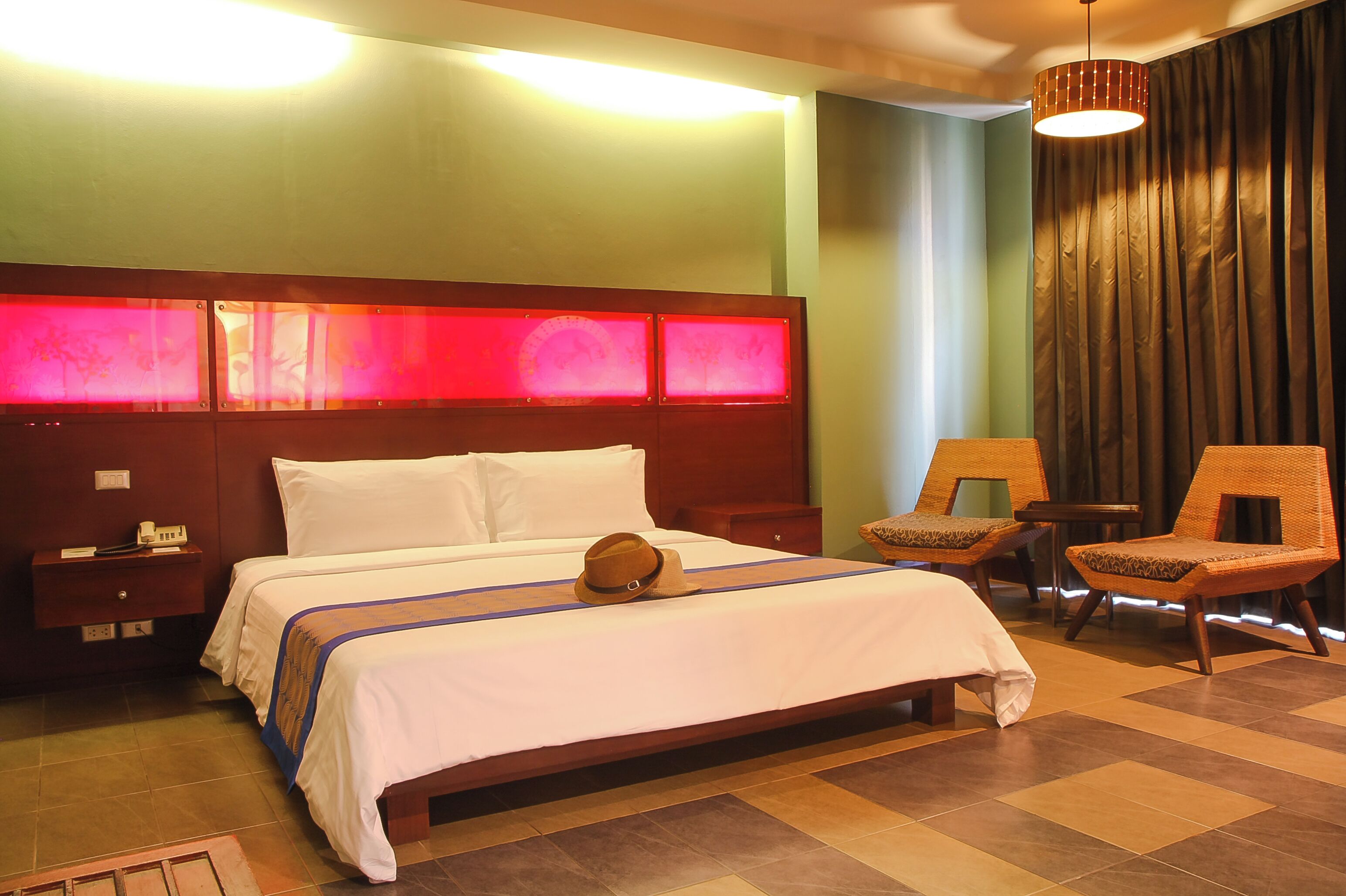 A hotel room with a large bed, a nightstand, two chairs, and a lamp.