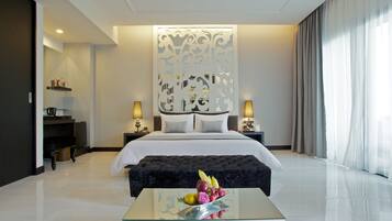 A modern hotel room with a large bed, a glass coffee table with fruit, a desk with a lamp, and a decorative wall panel.