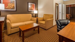 A hotel room with a sofa, armchair, and a small table. There is a lamp on a side table, and a door leading to another room. - Best Western Plus Easton Inn & Suites (Easton)