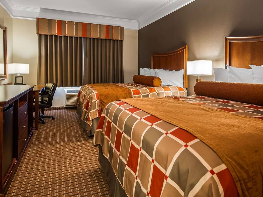 A hotel room with two beds, a desk, a chair, and a large window with curtains.