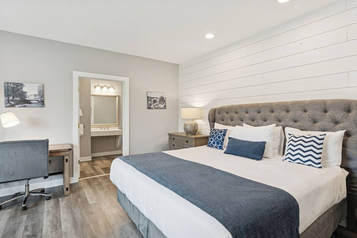A bedroom with a large bed, a desk, and a mirror.