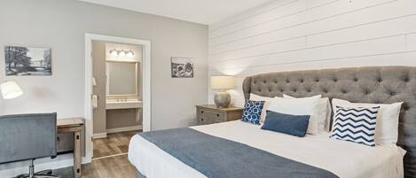 A bedroom with a large bed, a desk, and a mirror.