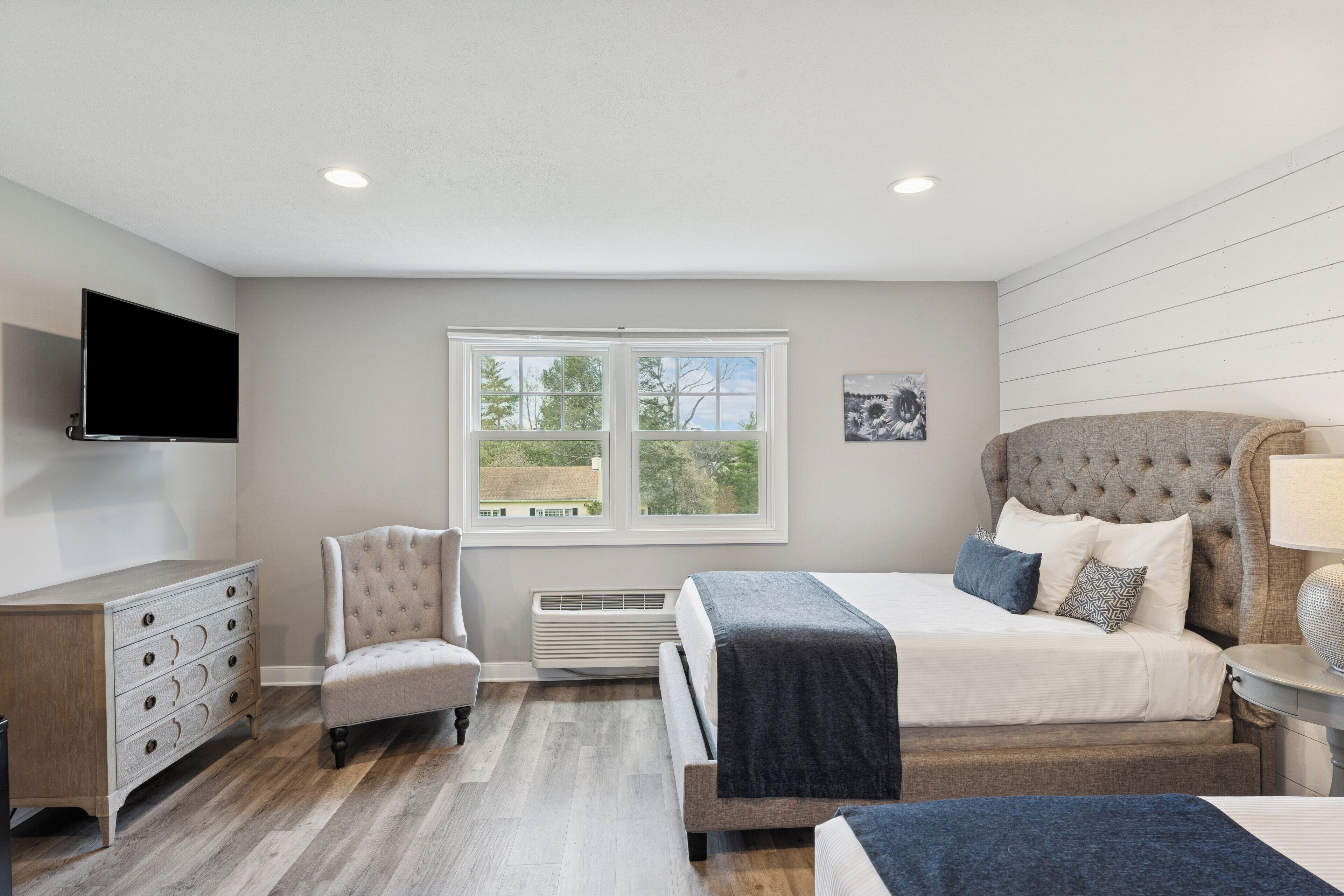 A bedroom with a bed, a chair, a dresser, a television, and a window with a view of trees.