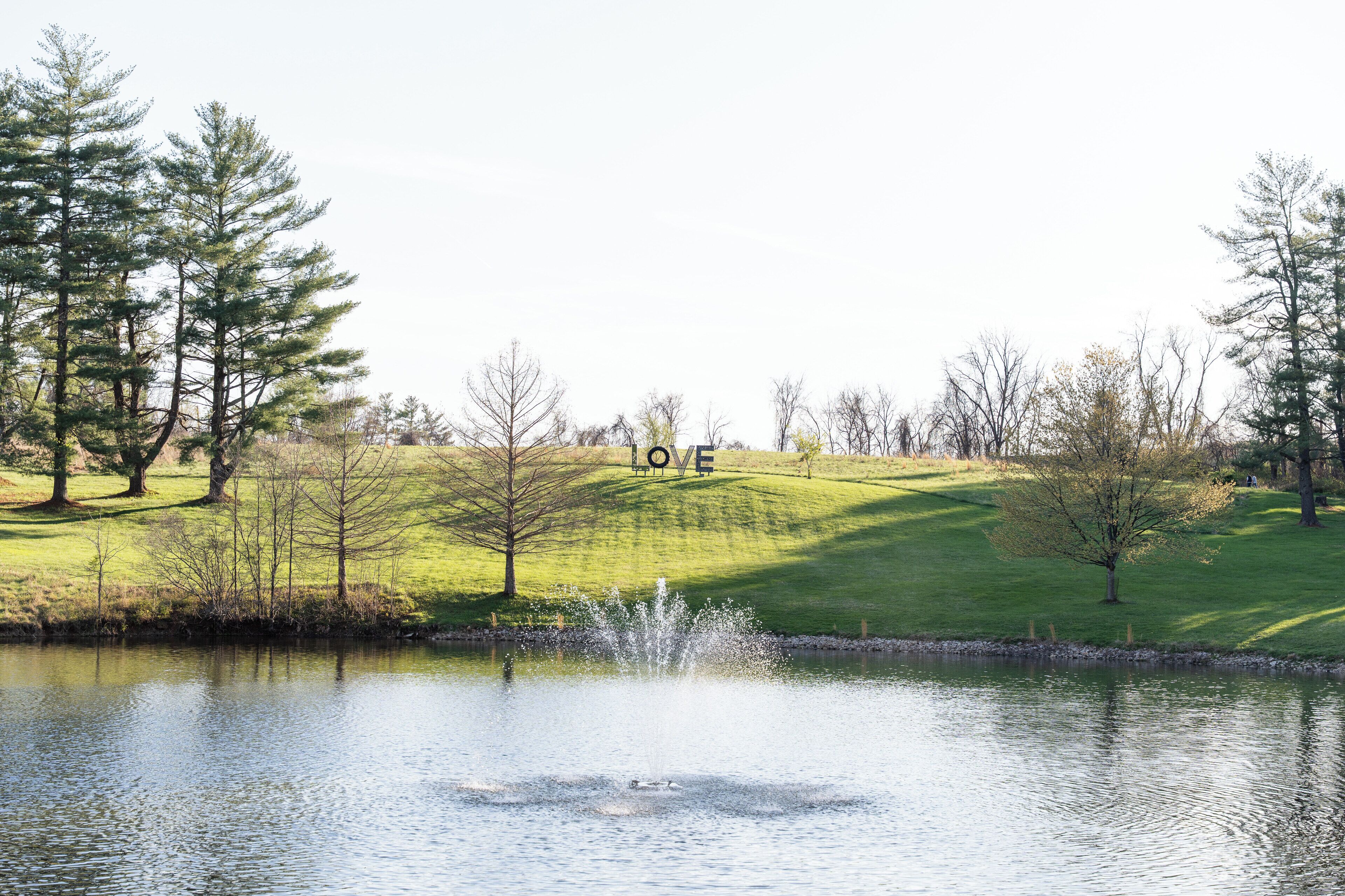 A serene park with a pond, trees, and a grassy hill.