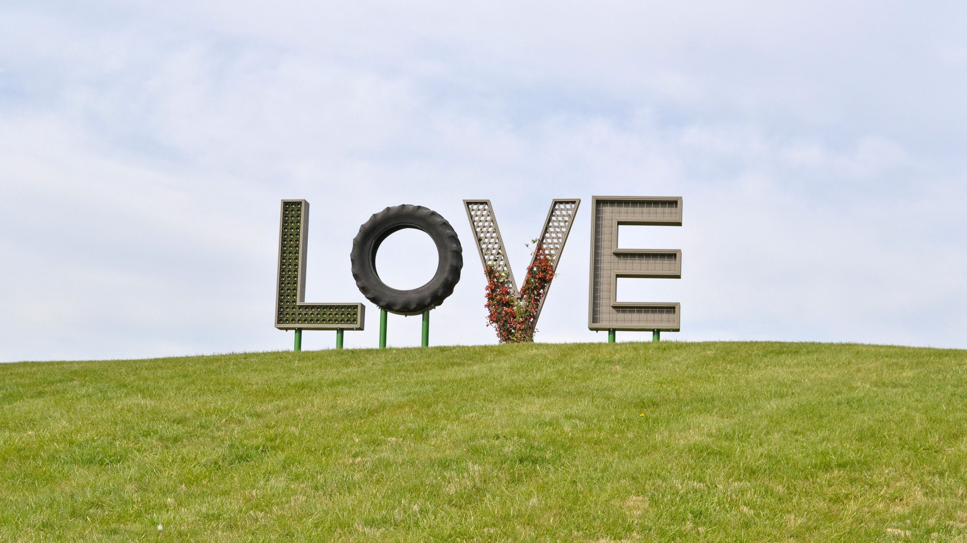 Une colline verdoyante sur laquelle sont disposées de grandes lettres formant le mot « AMOUR », et qui sont faites de différents matériaux.