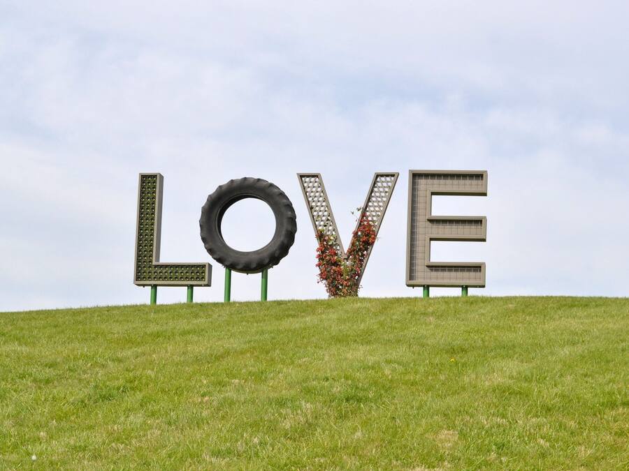 Une colline verdoyante sur laquelle sont disposées de grandes lettres formant le mot « AMOUR », et qui sont faites de différents matériaux.