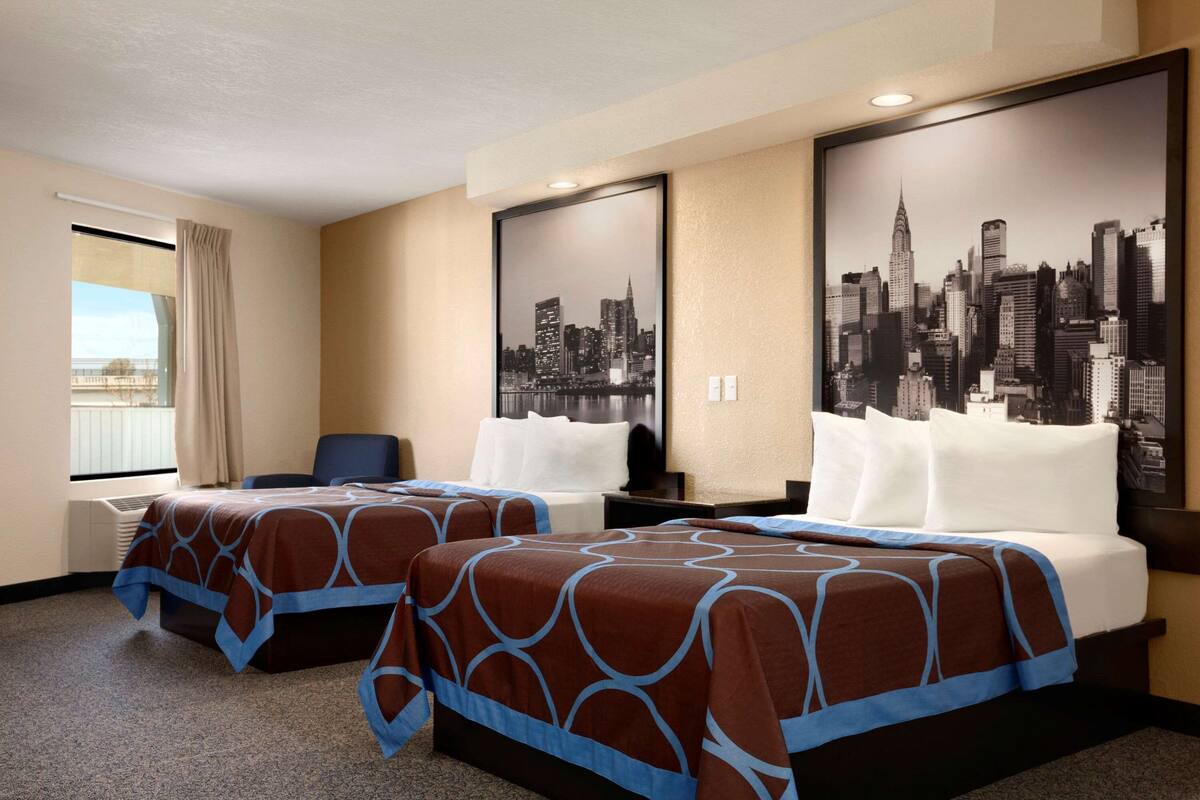 A hotel room with two beds, a desk, and a large cityscape poster on the wall.