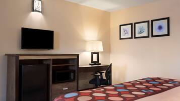 A hotel room with a bed, a desk with a flat-screen TV, a microwave, a refrigerator, a chair, a lamp, and three framed pictures on the wall.
