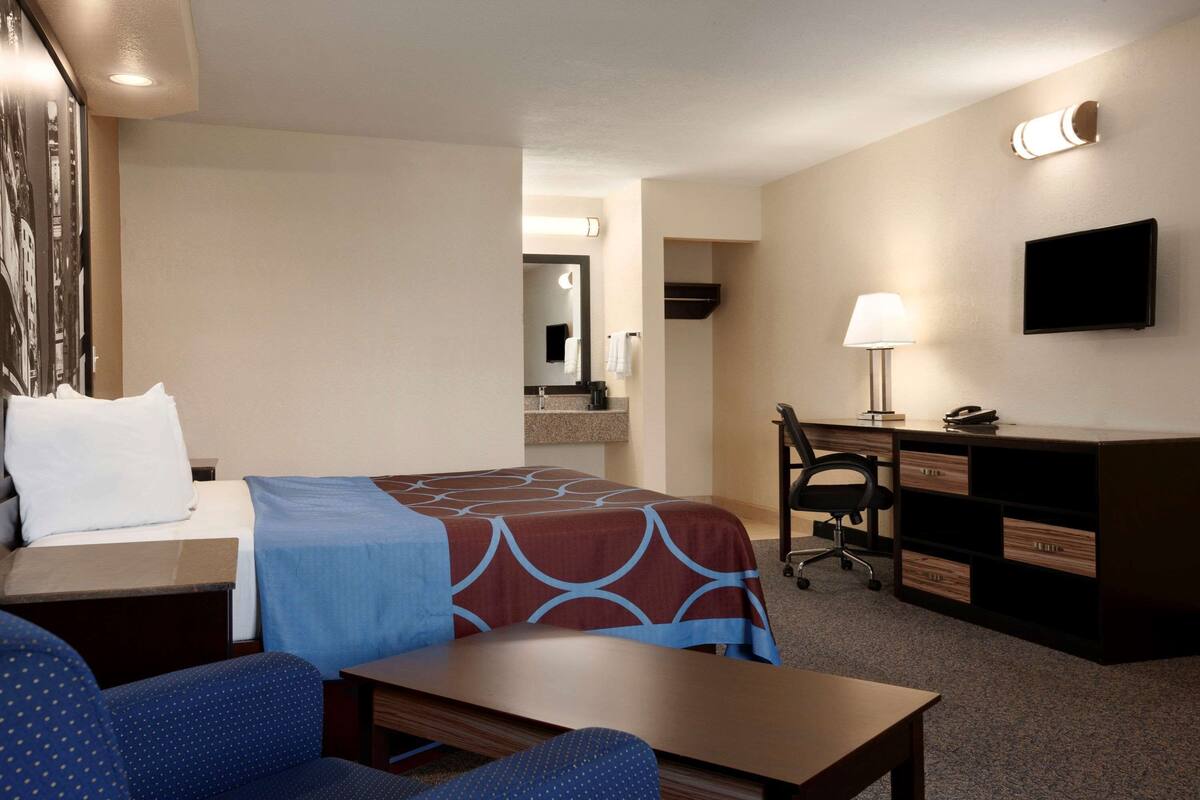 A hotel room with a bed, desk, chair, and a TV on the wall.