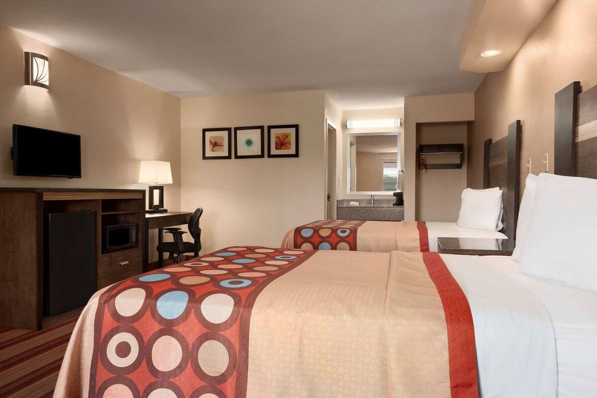A hotel room with two beds, a desk with a chair, a television, a microwave, and a refrigerator.