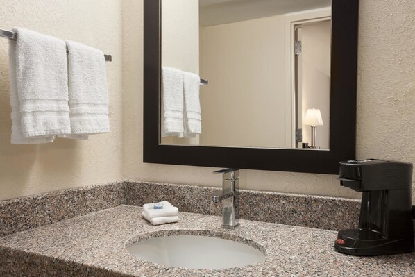 Un baño con encimera de granito, un lavabo, un espejo y una cafetera.