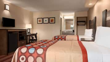 A hotel room with two beds, a desk with a TV, a microwave, and a refrigerator. There are three framed pictures on the wall.
