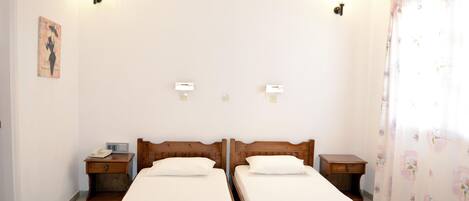 Una habitación con dos camas individuales, cabeceros de madera, mesitas de noche y una lámpara fijada a la pared.