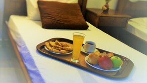 Un lit bien fait, avec un plateau contenant divers éléments pour le petit-déjeuner, notamment des toasts, des fruits et une boisson.