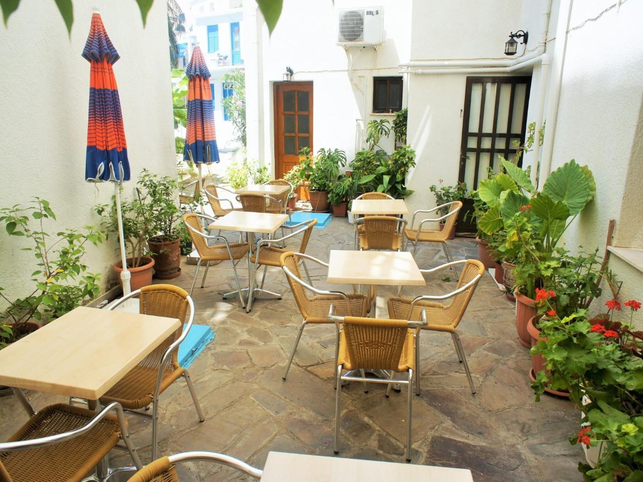 An outdoor patio area with wicker tables and chairs, potted plants, and a blue umbrella.