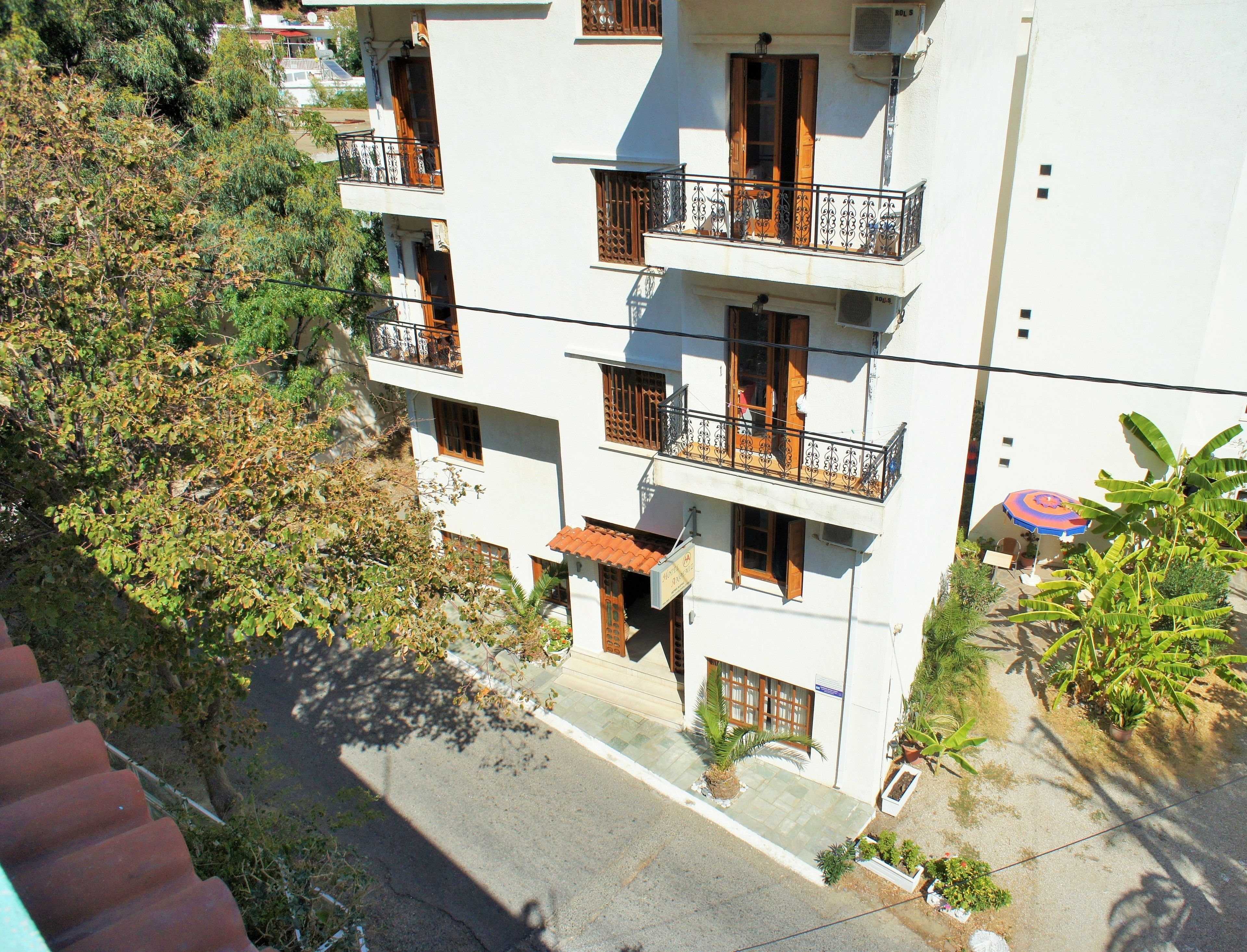 Un edificio de varios pisos con balcones, techo de tejas y abundante vegetación alrededor.