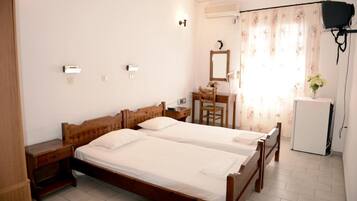 A bedroom with two wooden beds, a desk, a chair, a mirror, and a small refrigerator.