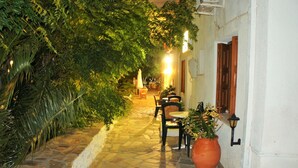 Un étroit sentier pavé de pierres menant à un patio aménagé avec des espaces de repos en plein air et des plantes en pot.