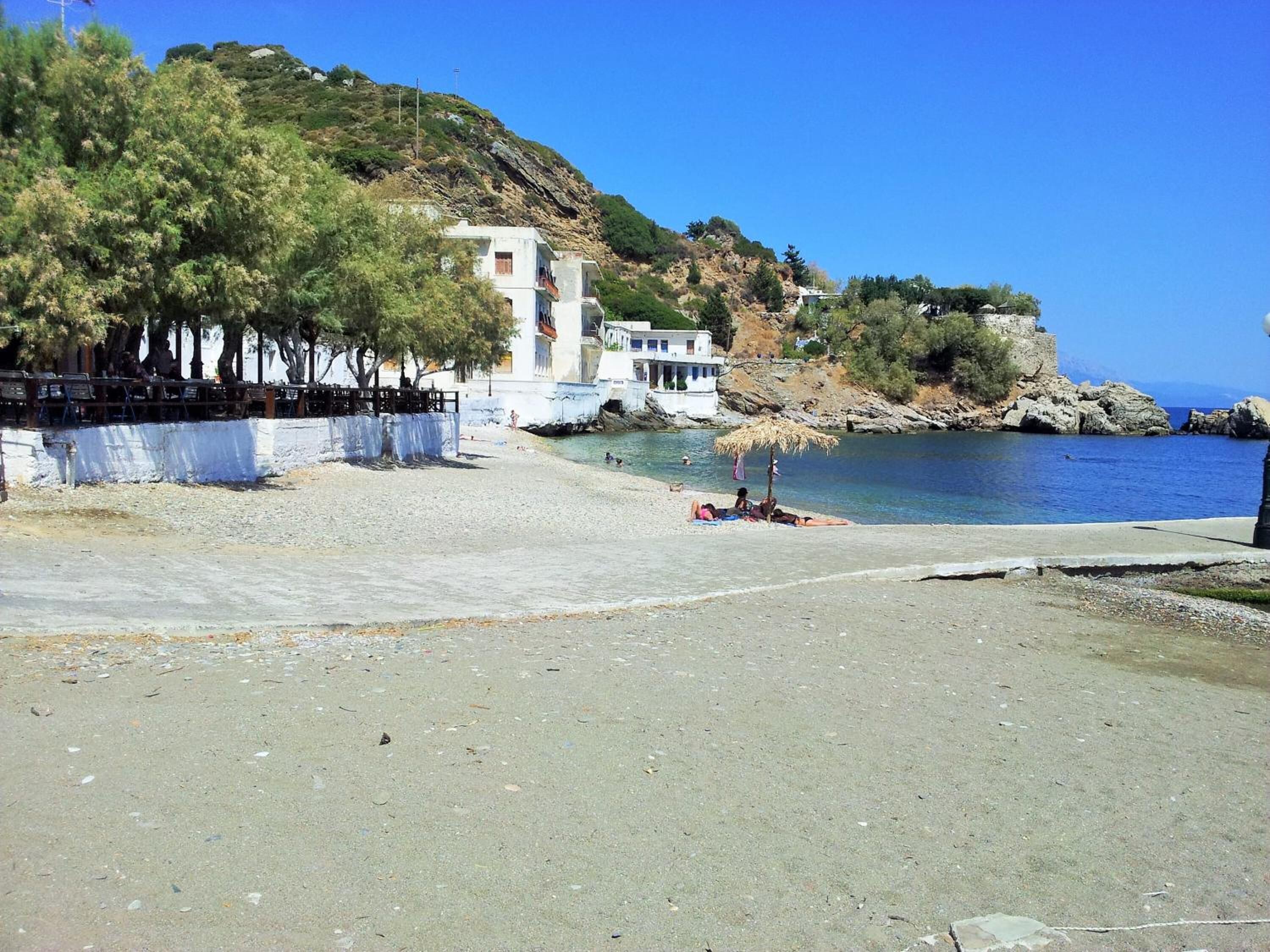 Una playa con un edificio blanco, árboles y un cielo azul despejado.