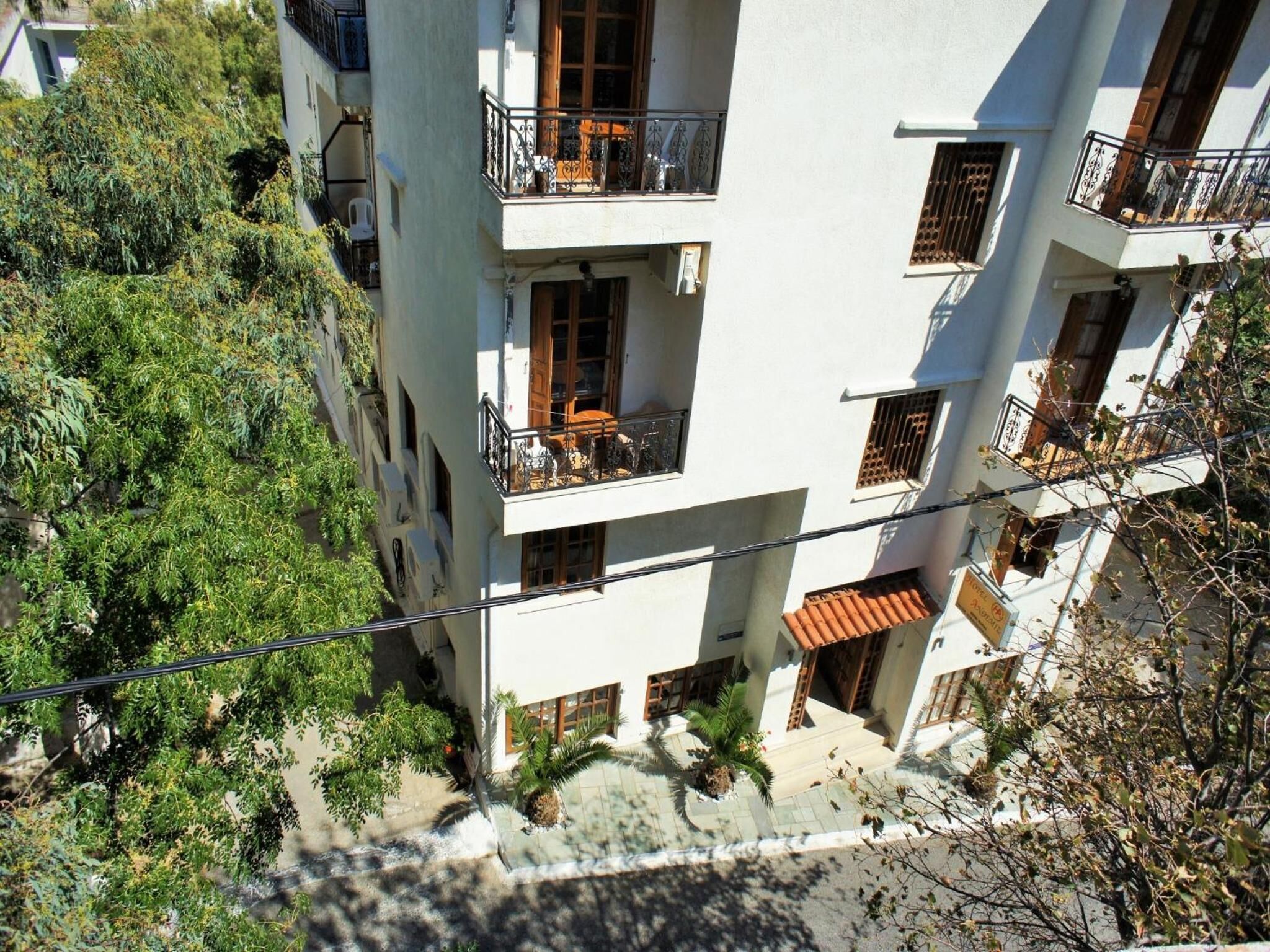 Un edificio de varios pisos con balcones, una entrada con tejas y abundante vegetación circundante.