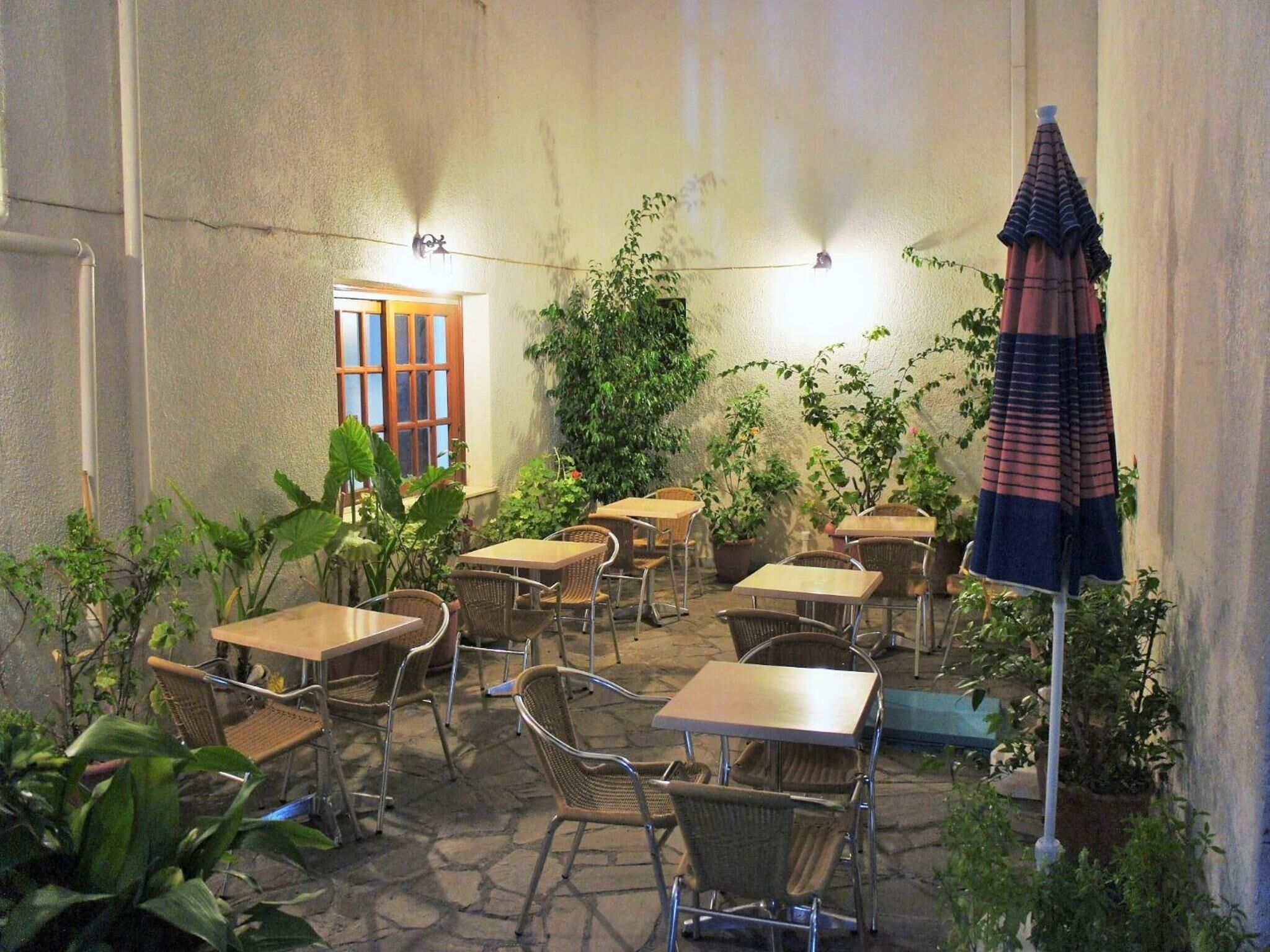 An outdoor patio with tables and chairs, surrounded by potted plants and a large umbrella.