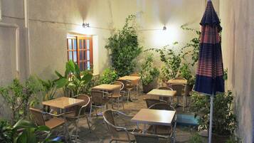 An outdoor patio with tables and chairs, surrounded by potted plants and a large umbrella.