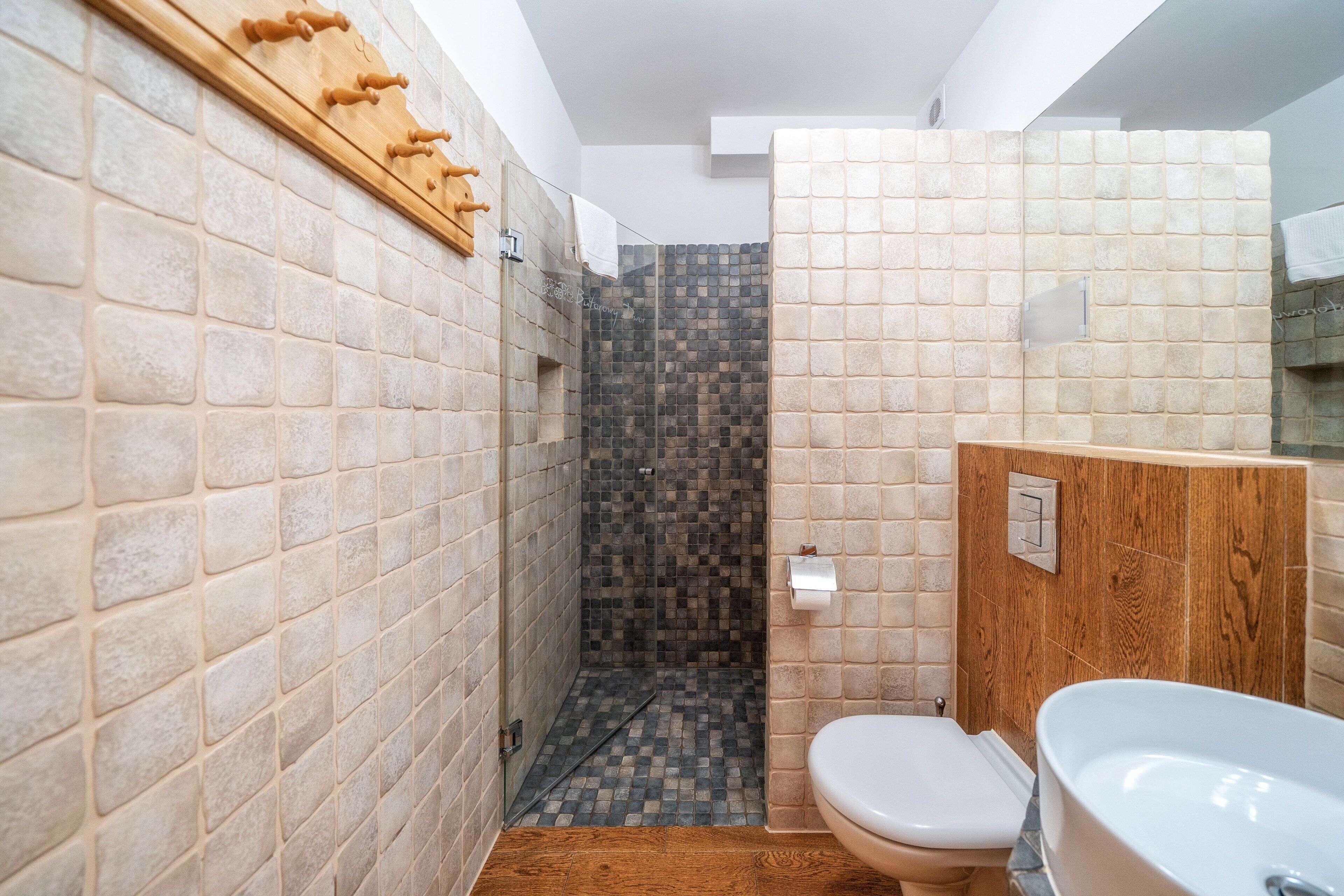 A bathroom with a shower, toilet, and sink, featuring tiled walls and wooden accents.