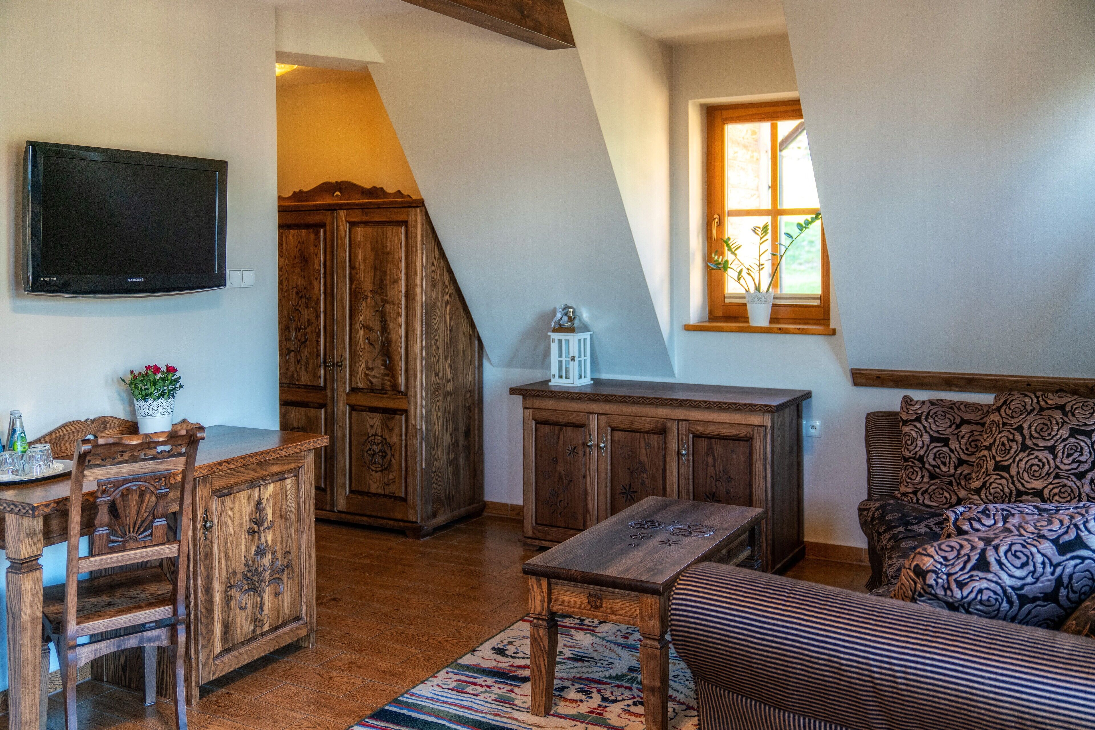 A cozy living room with a wooden table, a sofa, and a TV mounted on the wall.