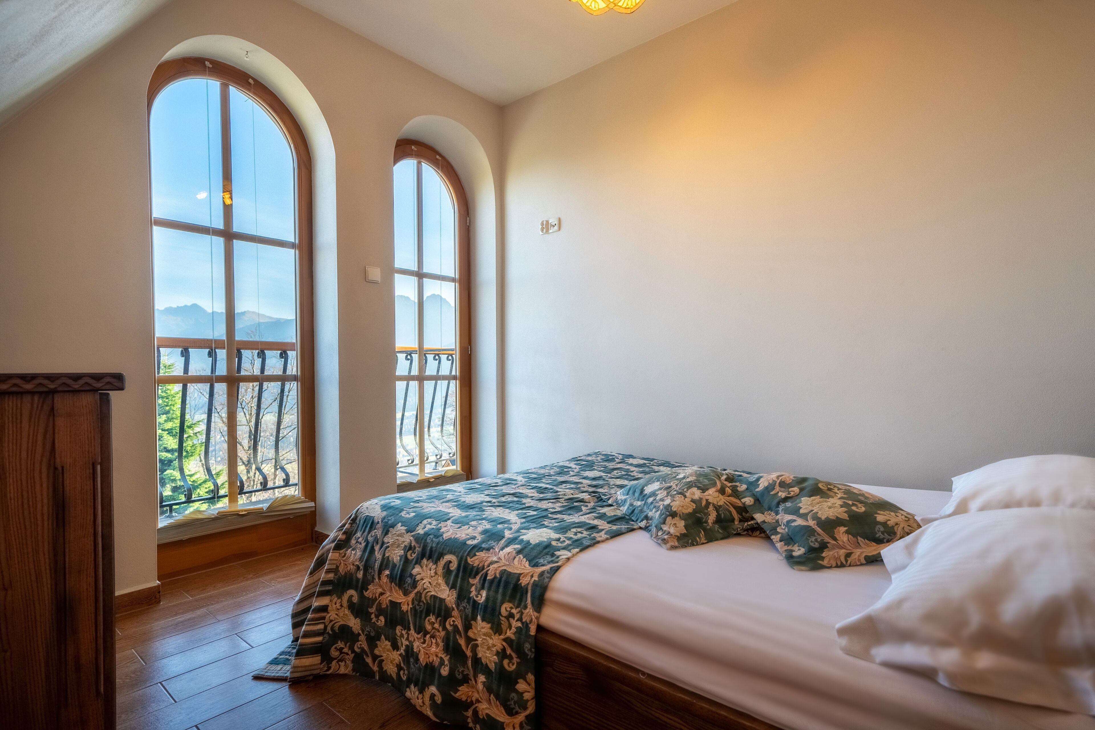 A bedroom with a large bed, two windows, and a view of mountains.