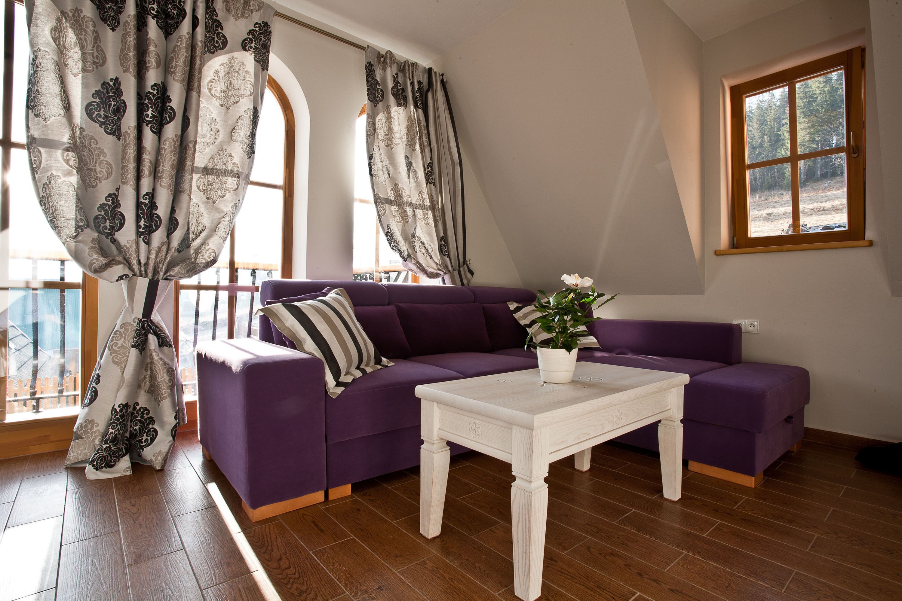 A living room with a purple sofa, a white coffee table, and a window with a view of trees.