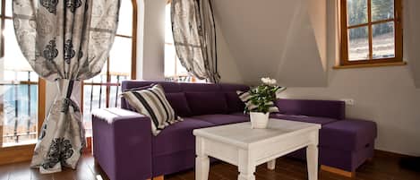 A living room with a purple sofa, a white coffee table, and a window with a view of trees.