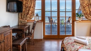 Una habitación con un escritorio de madera, una cama con colcha floral y un balcón con vistas a montañas.