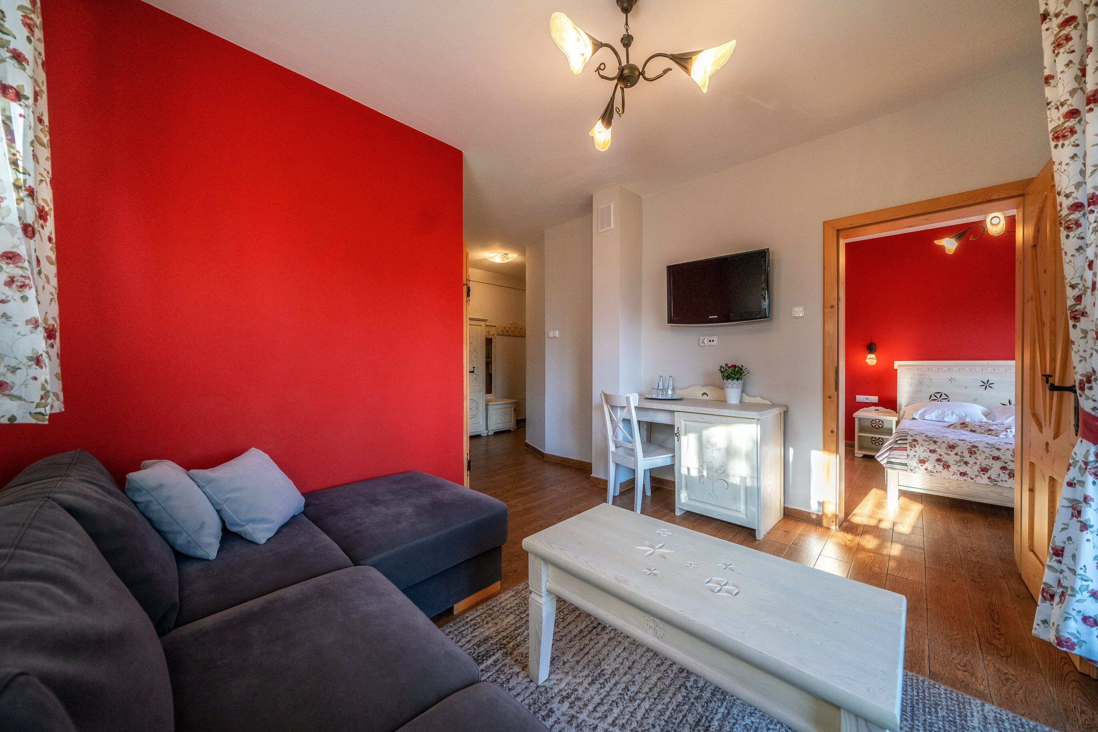 Una sala moderna con una pared de acento roja, un sofá gris, una mesa de centro blanca y un televisor montado en la pared.