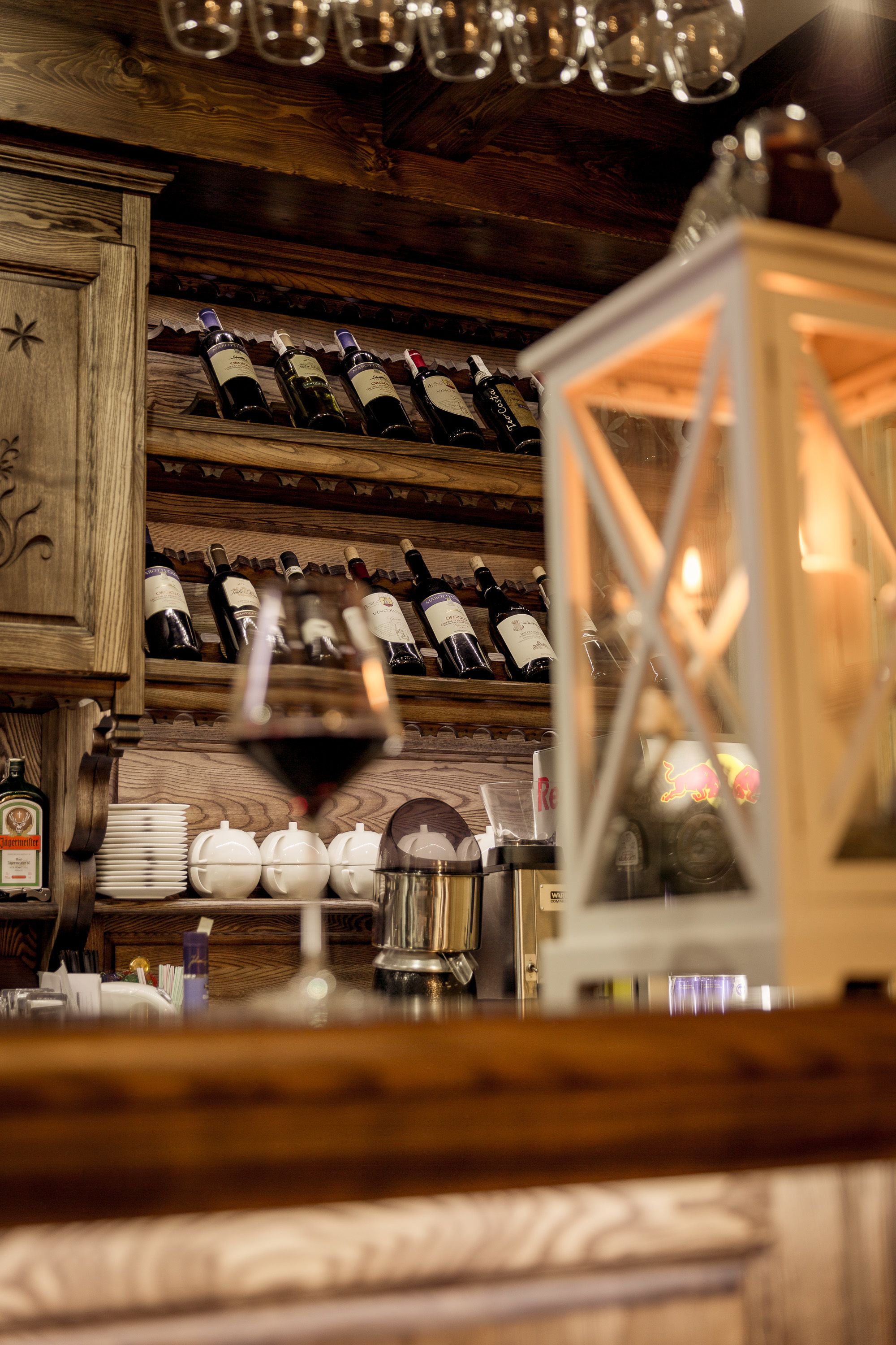 A wooden wine rack with bottles, a wine glass, and a lantern.
