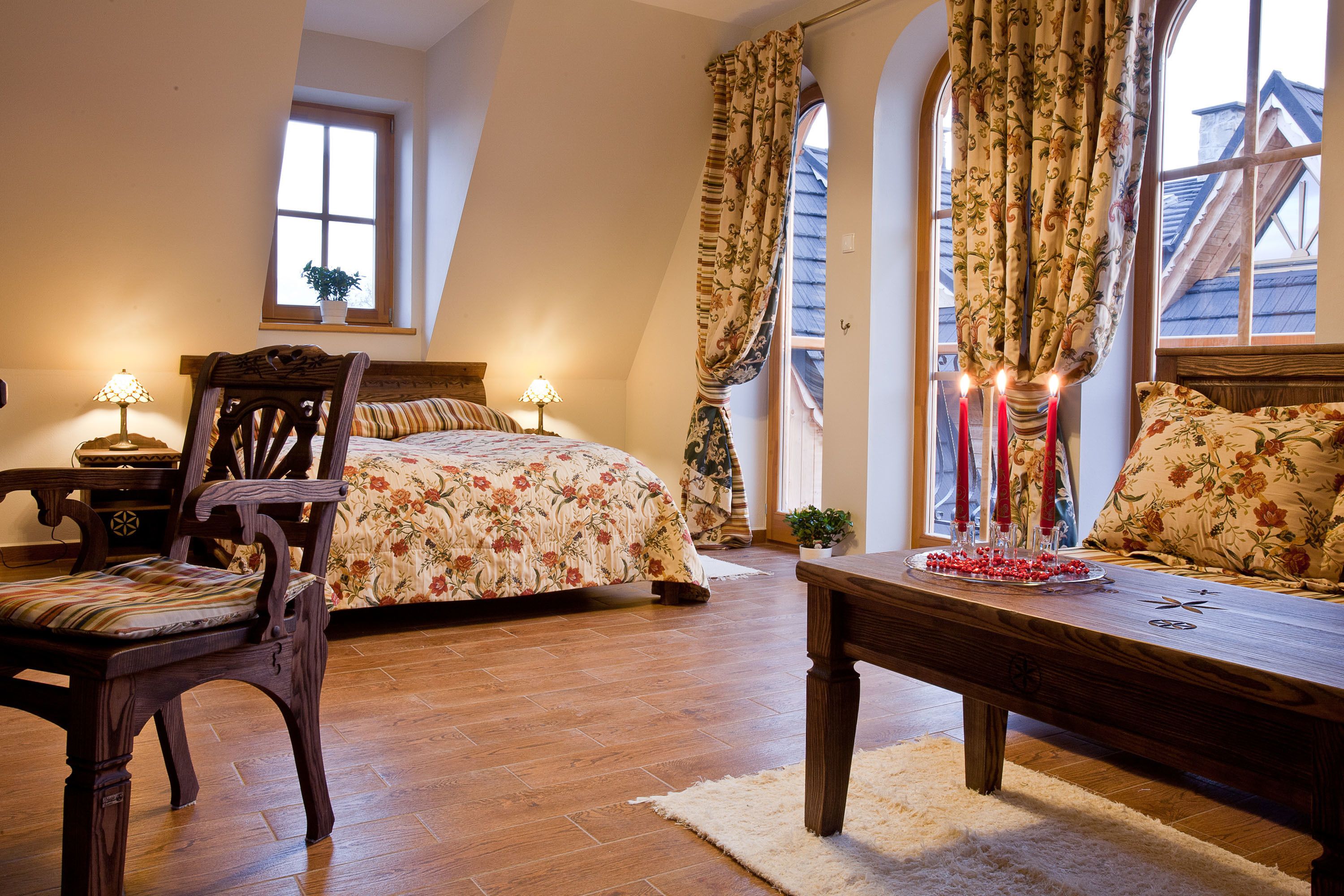 A bedroom with a wooden bed, a wooden chair, a table, and a window with curtains.