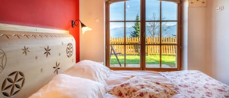 Un dormitorio con un ventanal grande, un cabecero de madera con diseños geométricos y una colcha con estampado floral.