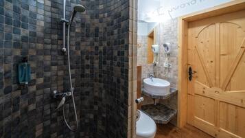 Un bagno con doccia, WC e lavandino, caratterizzato da una parete in pietra e una porta in legno.