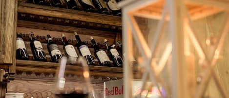 A wine rack with multiple bottles, a Red Bull refrigerator, and a glass of red wine.